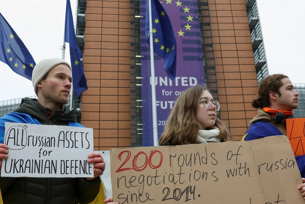 Люди тримають плакати під час демонстрації біля будівлі Європейської комісії на підтримку використання заморожених російських активів для фінансування України на тлі російської агресії проти України, Брюссель, Бельгія, 17 грудня 2025 року.