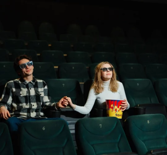 закохані чоловік та дівчина тримаються за руку у кінозалі