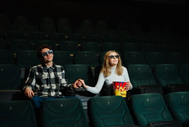 закохані чоловік та дівчина тримаються за руку у кінозалі