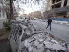 іранець йде по дорозі біля зруйнованих будівель та автівок