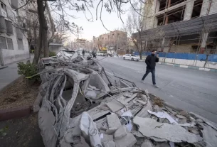 іранець йде по дорозі біля зруйнованих будівель та автівок