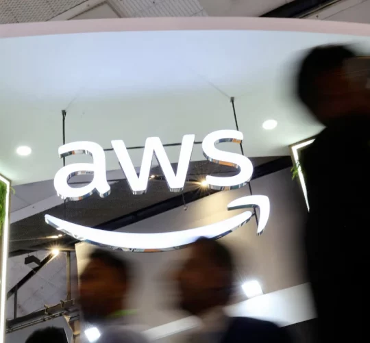 Люди проходять повз логотип Amazon Web Services (AWS) на стенді компанії на виставці India Mobile Congress 2025