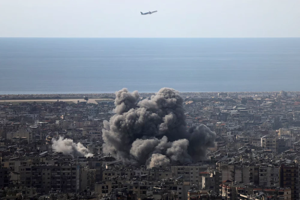 Літак летить, коли клуби диму піднімаються після ізраїльського удару по південних передмістях Бейрута після ескалації між "Хезболлою" та Ізраїлем на тлі американо-ізраїльського конфлікту з Іраном