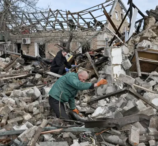Двоє чоловіків розбирають залишки будинку, зруйнованого внаслідок російського авіаудару на околиці Запоріжжя