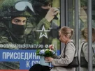 росіянка сидить на зупинці з плакатом на якому заклик до приєднання до військової служби