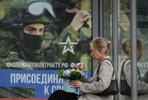 росіянка сидить на зупинці з плакатом на якому заклик до приєднання до військової служби