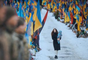 молода жінка йде з малюком на руках повз могили загиблих українських воїнів