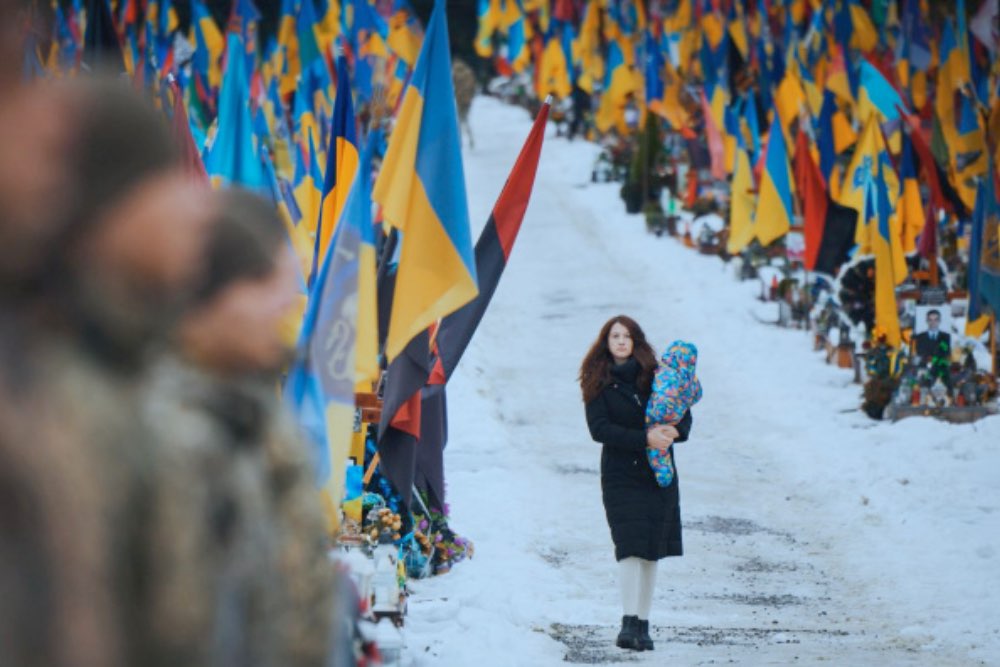 молода жінка йде з малюком на руках повз могили загиблих українських воїнів
