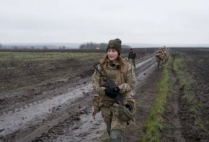 українська жінка військова йде по переду з автоматом по українському полі