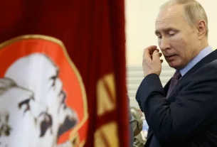 Володимир Путін проходить біля прапорів з фото Леніна та Сталіна