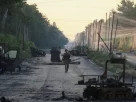 військовий йде по дорозі з розбитою технікою