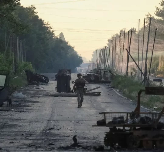 військовий йде по дорозі з розбитою технікою