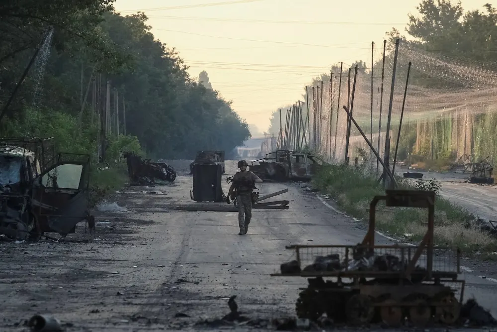 військовий йде по дорозі з розбитою технікою