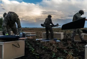 Люди в тактичному спорядженні збирають дрони на сільському полі під похмурим небом