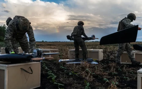 Люди в тактичному спорядженні збирають дрони на сільському полі під похмурим небом