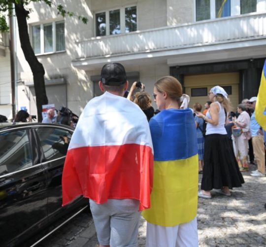 люди обгорнуті у прапори Польщі та України стоять поручь