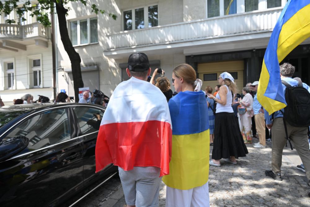 люди обгорнуті у прапори Польщі та України стоять поручь