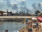 Місцеві жителі та гості міста Одеса відпочивають на пляжі, коли піднімається дим від пожежі, що спалахнула внаслідок російського ракетного удару 29 липня
