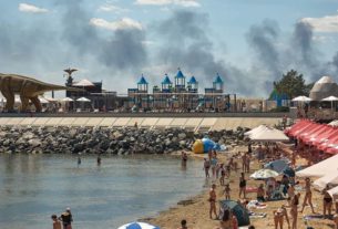 Місцеві жителі та гості міста Одеса відпочивають на пляжі, коли піднімається дим від пожежі, що спалахнула внаслідок російського ракетного удару 29 липня