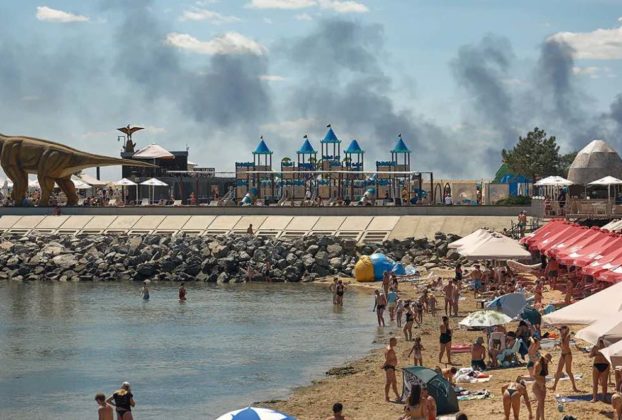 Місцеві жителі та гості міста Одеса відпочивають на пляжі, коли піднімається дим від пожежі, що спалахнула внаслідок російського ракетного удару 29 липня