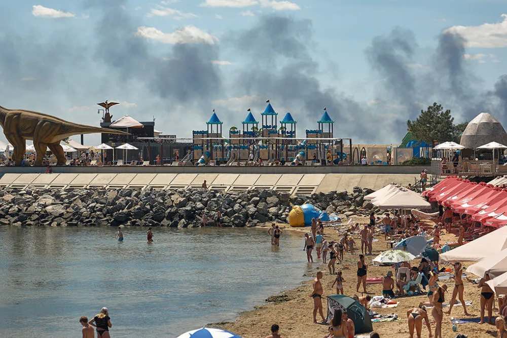 Місцеві жителі та гості міста Одеса відпочивають на пляжі, коли піднімається дим від пожежі, що спалахнула внаслідок російського ракетного удару 29 липня