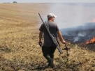 Фермер тримає в руках частину російського дрона, який він збив з рушниці, спостерігаючи за тим, як горить поле після повітряного удару в Харківській області, у середу, 5 серпня 2026 року