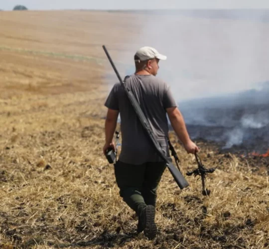 Фермер тримає в руках частину російського дрона, який він збив з рушниці, спостерігаючи за тим, як горить поле після повітряного удару в Харківській області, у середу, 5 серпня 2026 року