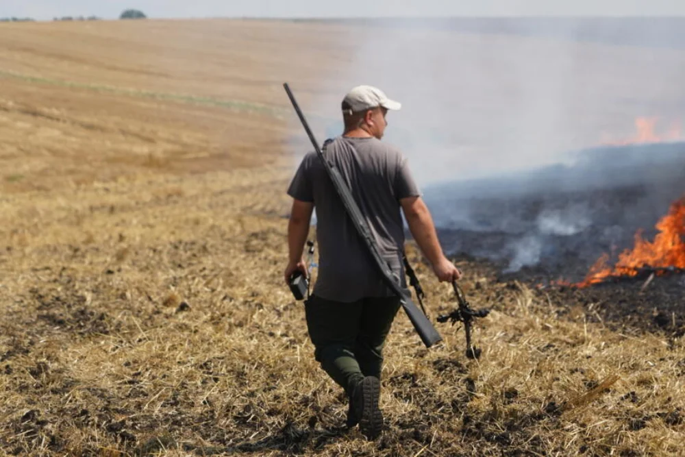 Фермер тримає в руках частину російського дрона, який він збив з рушниці, спостерігаючи за тим, як горить поле після повітряного удару в Харківській області, у середу, 5 серпня 2026 року