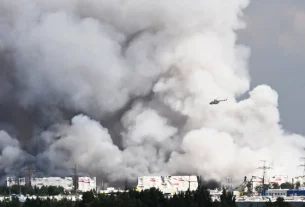 Вертоліт пролітає повз стовпи диму, що піднімаються з російського складу електронної комерції поблизу Санкт-Петербурга після удару українського дрона 24 липня 2026 року