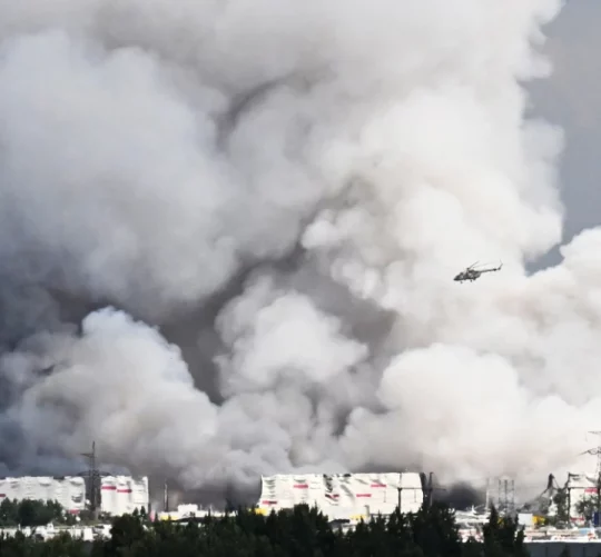 Вертоліт пролітає повз стовпи диму, що піднімаються з російського складу електронної комерції поблизу Санкт-Петербурга після удару українського дрона 24 липня 2026 року