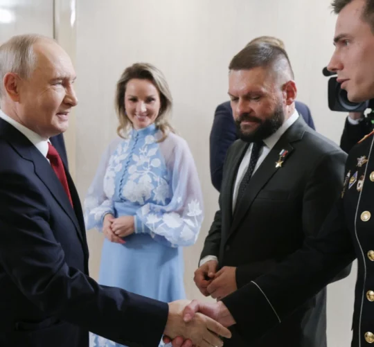 Президент Росії Володимир Путін (ліворуч) вітає Владислава Головіна (праворуч) під час зустрічі з керівниками політичної партії «Єдина Росія» у присутності уповноваженої президента з прав дітей Марії Львової-Белової (у центрі) та військового кореспондента Євгена Поддубного (другий праворуч) у Москві в суботу, 5 вересня 2026 року