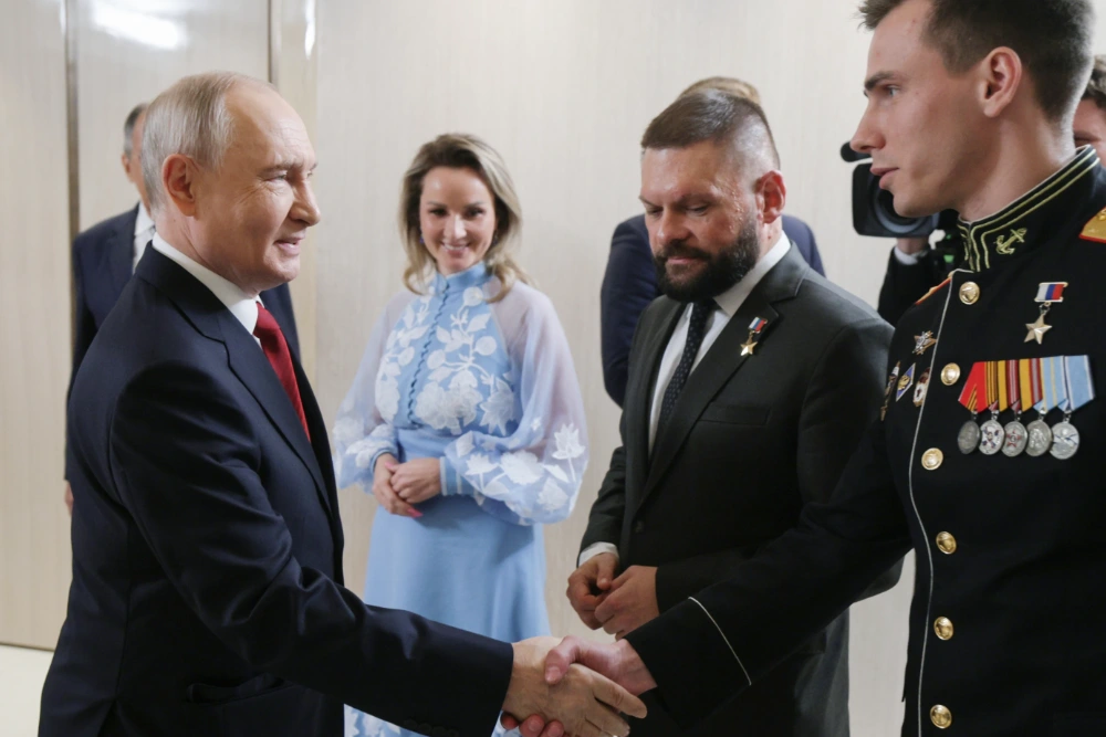 Президент Росії Володимир Путін (ліворуч) вітає Владислава Головіна (праворуч) під час зустрічі з керівниками політичної партії «Єдина Росія» у присутності уповноваженої президента з прав дітей Марії Львової-Белової (у центрі) та військового кореспондента Євгена Поддубного (другий праворуч) у Москві в суботу, 5 вересня 2026 року