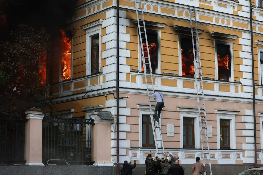 Люди допомагають чоловікові евакуюватися з Національної академії наук у Києві після удару російського безпілотника, що стався у понеділок