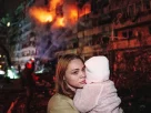 Жінка тримає на руках свою доньку, стоячи перед багатоповерховим житловим будинком, пошкодженим внаслідок російського ракетного удару в Києві, Україна