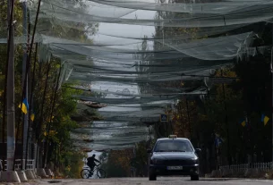 Місцевий житель їде на велосипеді під сітками проти дронів, натягнутими над вулицею, під час місцевого перемир’я, пов’язаного з місією з доставки гуманітарної допомоги в Олешках, Херсонська область, Україна, у середу, 28 жовтня 2026 року
